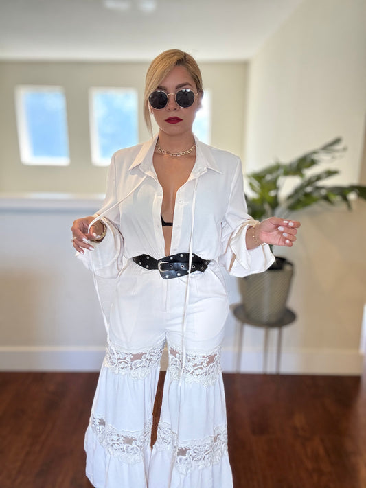 White jumpsuit with button-front shirt, long sleeves, lace trim hem, and dark belt