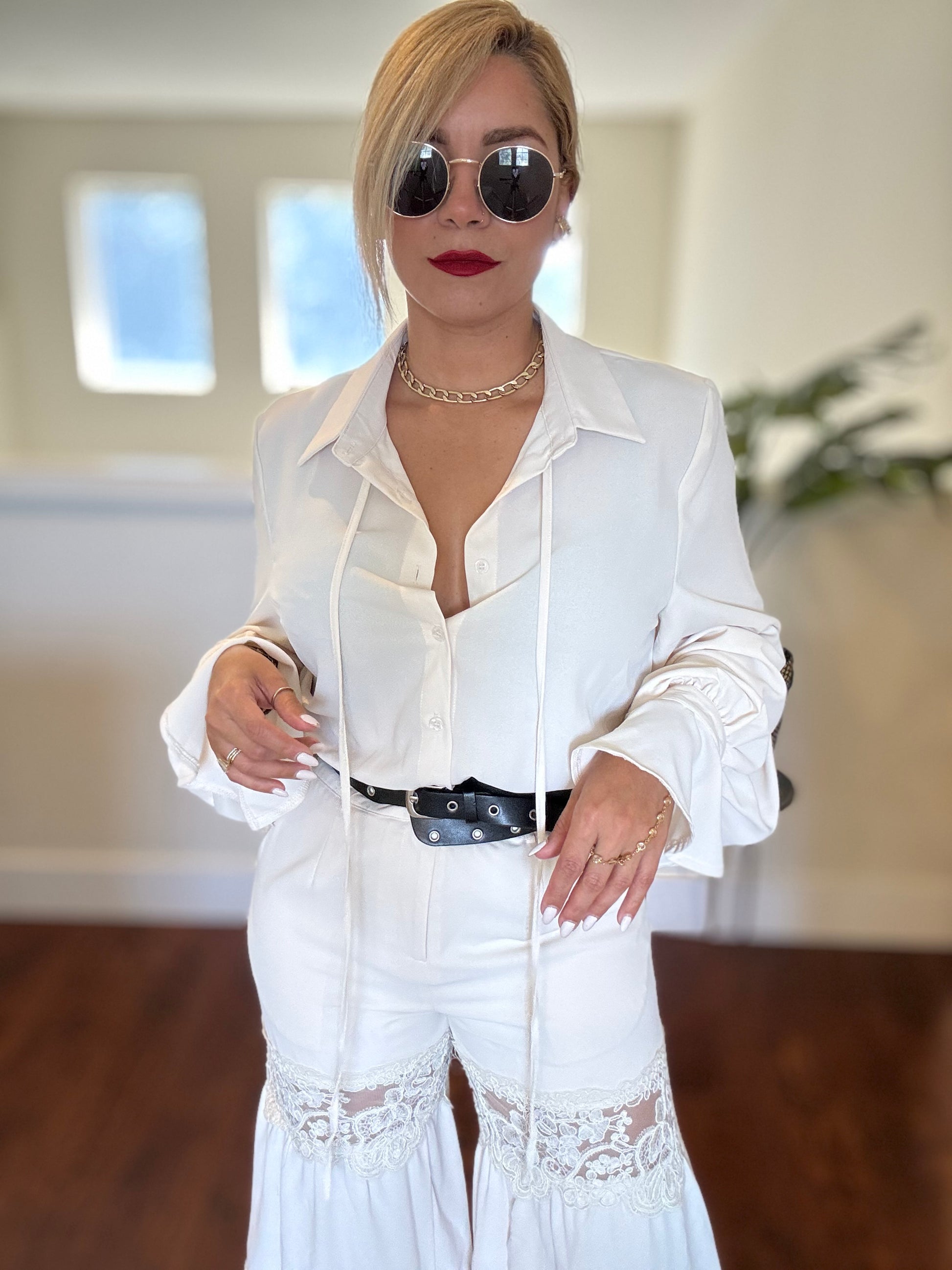 White collared jumpsuit with button front, lace panels at hips, and black studded belt