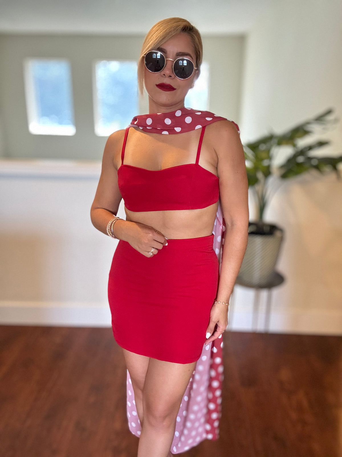Red bralette-style crop top and mini skirt with polka-dot sheer wrap trailing behind.