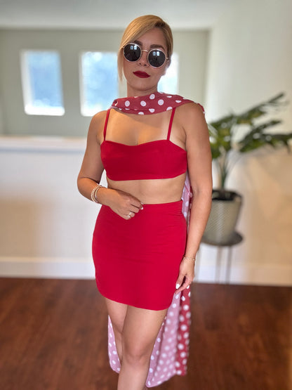 Red bralette-style crop top and mini skirt with polka-dot sheer wrap trailing behind.