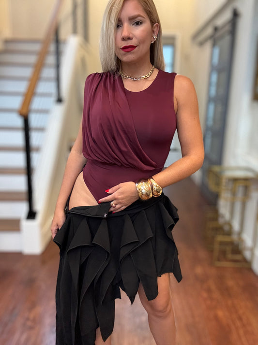 Burgundy sleeveless bodysuit with black ruffled layered skirt, hands at waist