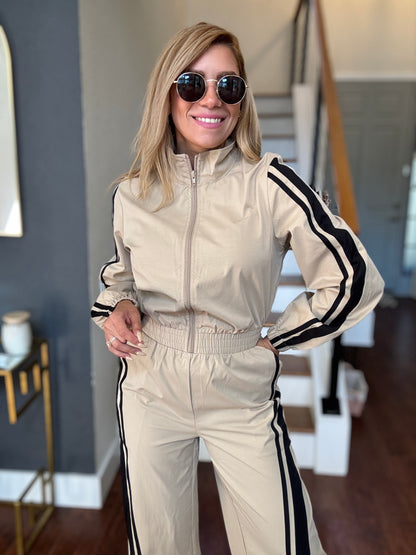 Bianca Fly jumpsuit in beige with hooded zip front, gathered waist, and black side stripes