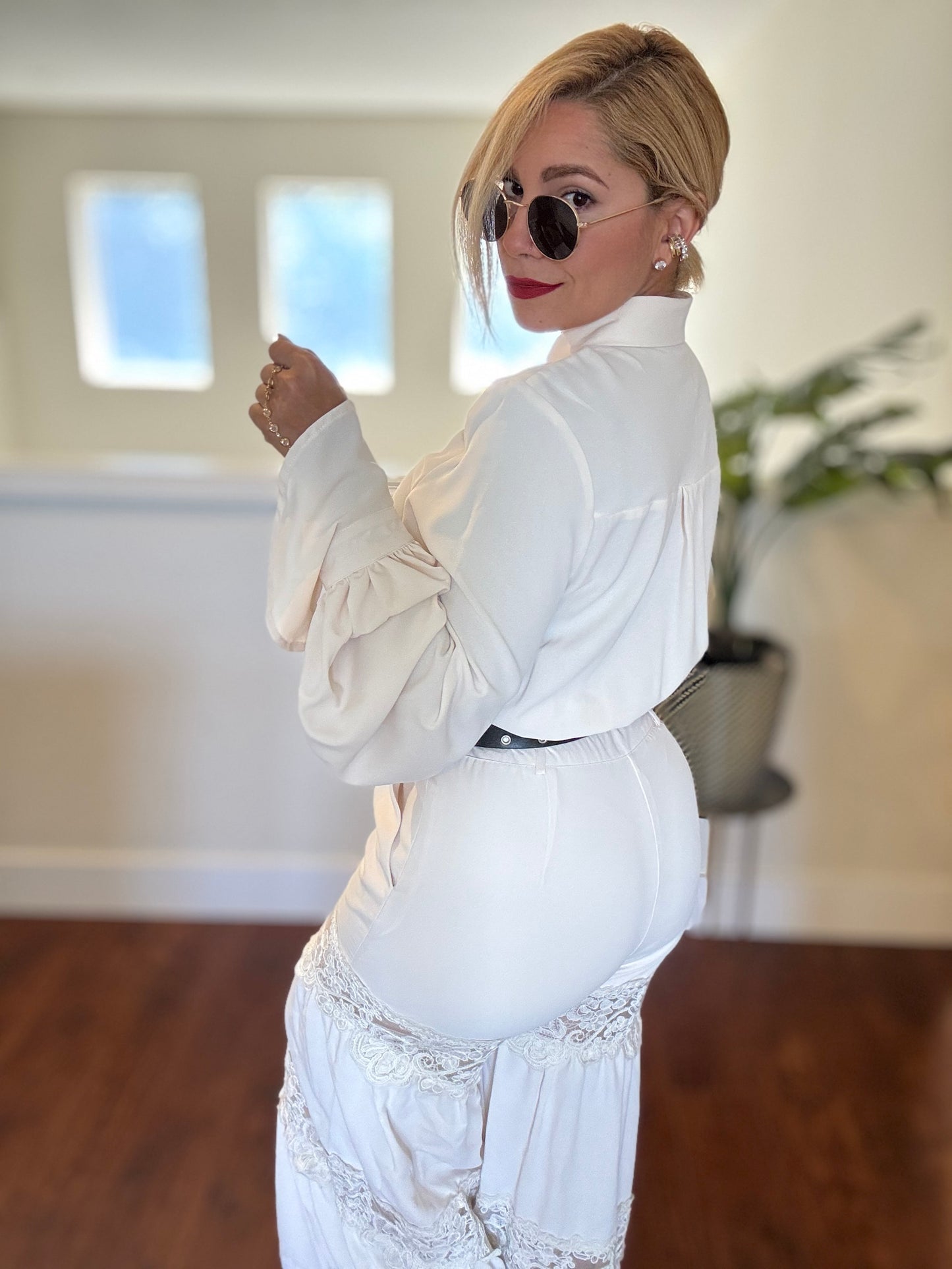 White high-collar jumpsuit with lace trim, long sleeves, and tied neck detail