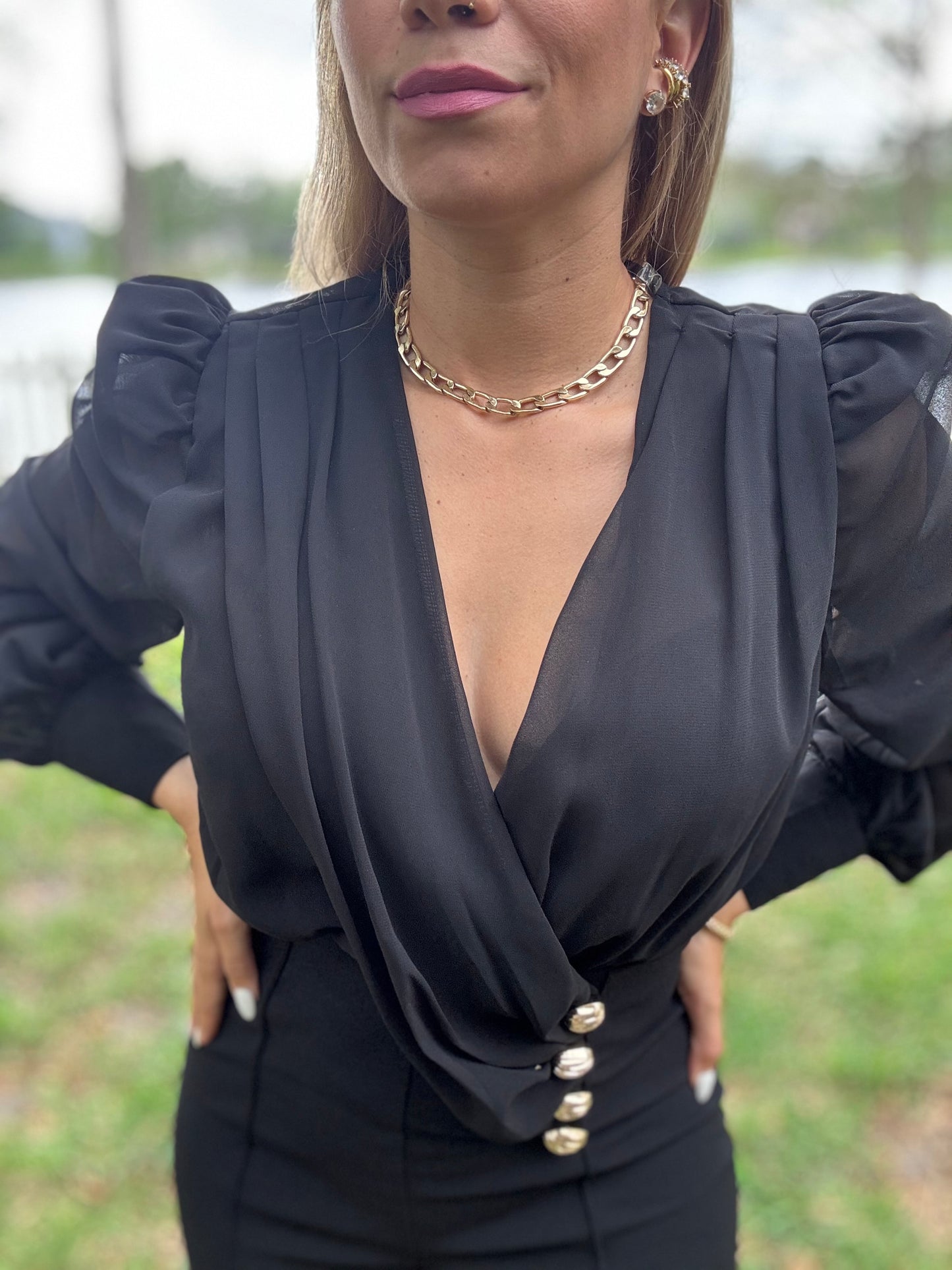 Black V-neck jumpsuit close-up with puff sleeves and gold button waist detail