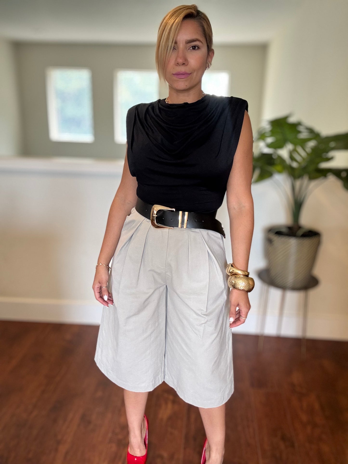 Black sleeveless top with draped neckline and white belted shorts, standing pose