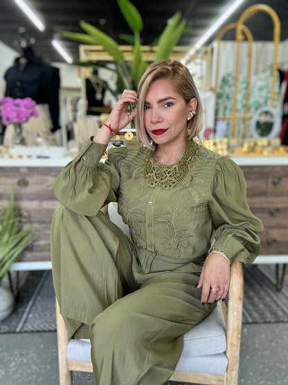 Olive green lace yoke button blouse and matching wide-leg pants, seated with arm raised