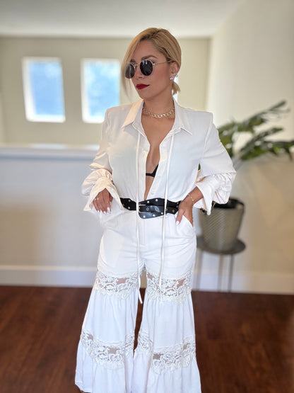 White lace-trim jumpsuit with long sleeves, deep V opening, and tiered hem detail