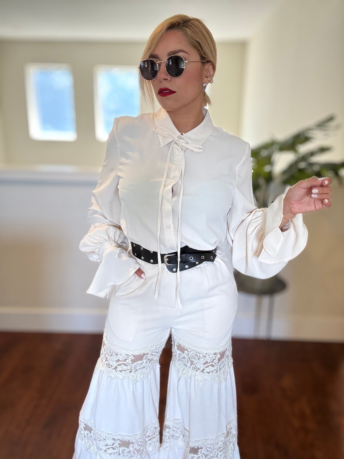 White button-up jumpsuit with deep V neckline, lace trim, and black belt with studs