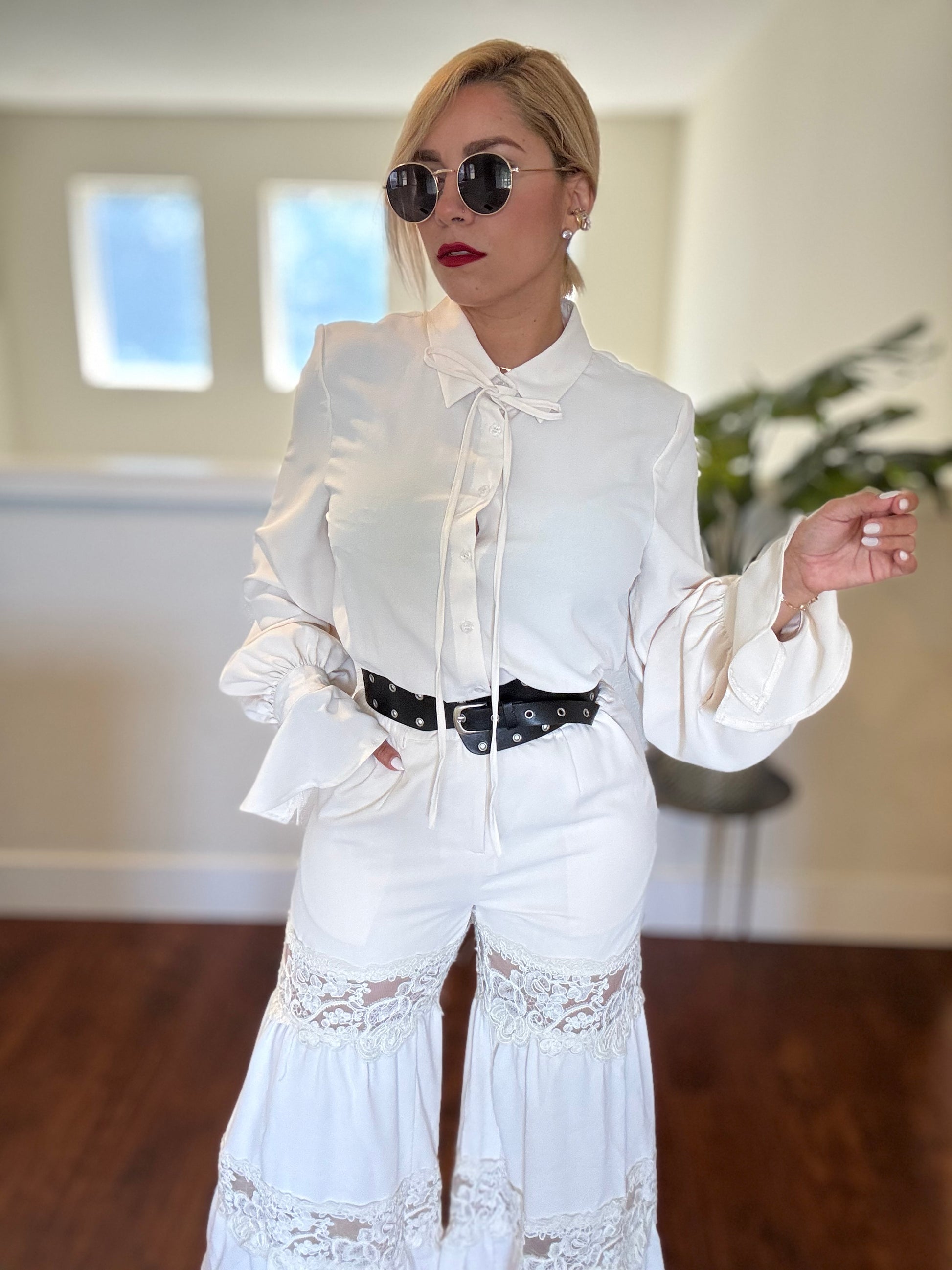 White button-up jumpsuit with deep V neckline, lace trim, and black belt with studs