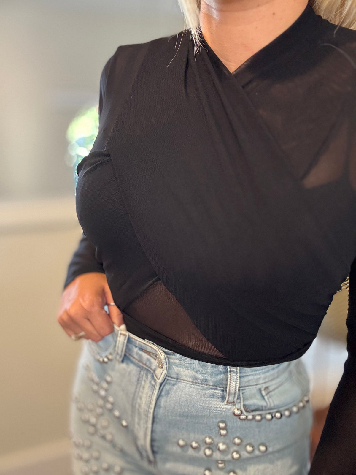 Black draped bodysuit close-up with V neckline and sheer long sleeves